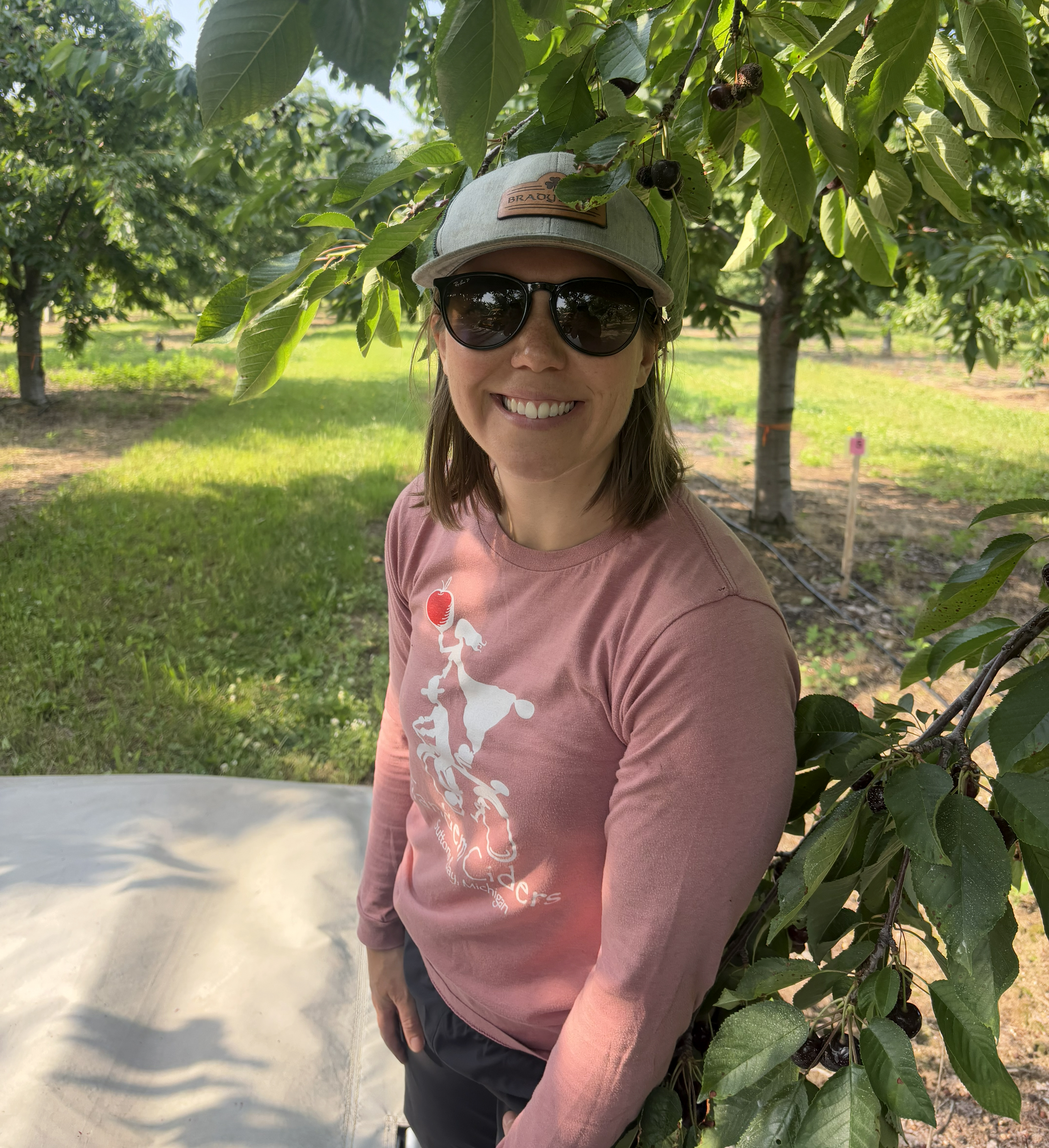 A woman smiling and standing in a cherry orchard.